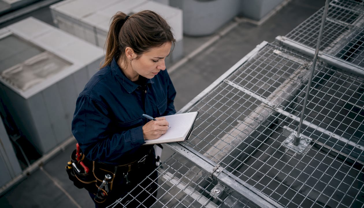 Une technicienne procède à l’inspection d’une cage grillagée installée sur le toit.
