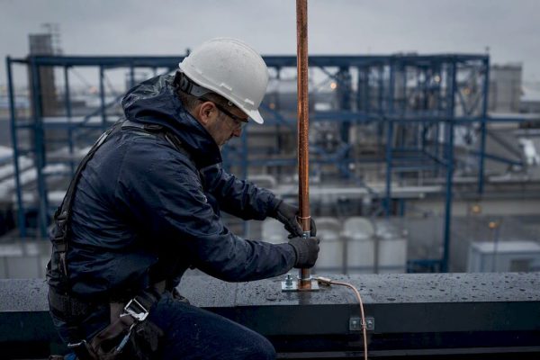 Technician installing lightning rod on industrial rooftop
