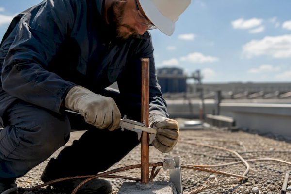 Un technicien effectue des mesures sur une prise de terre pour paratonnerre à l'extérieur.