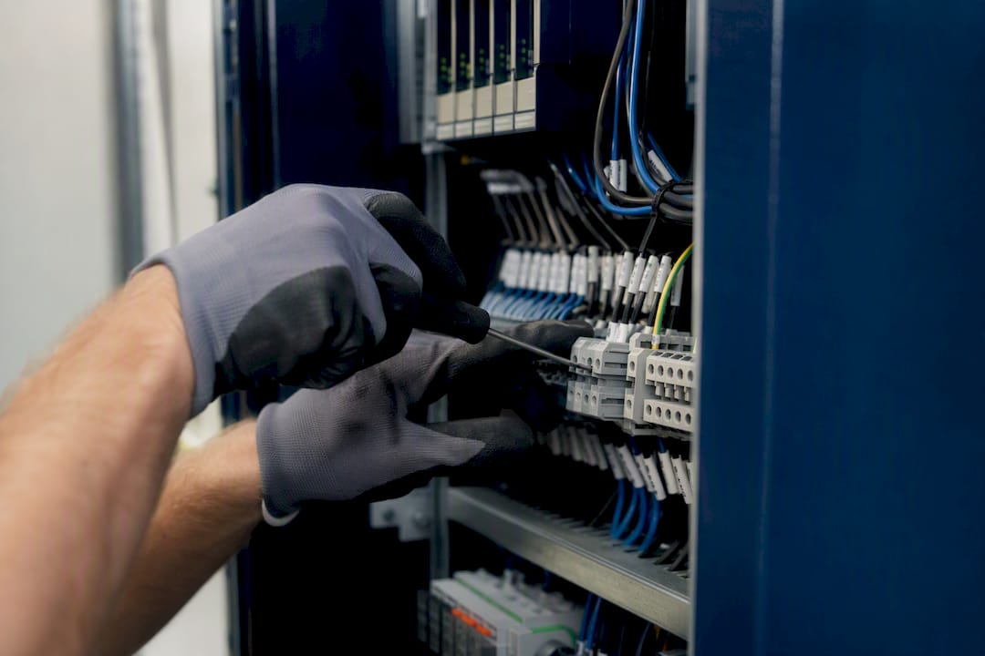 Mains de technicien serrant un bornier dans une armoire électrique